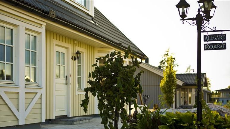 Gult trähus med ett Yale dörrlås, vita knutar, trädgård med smideslampa